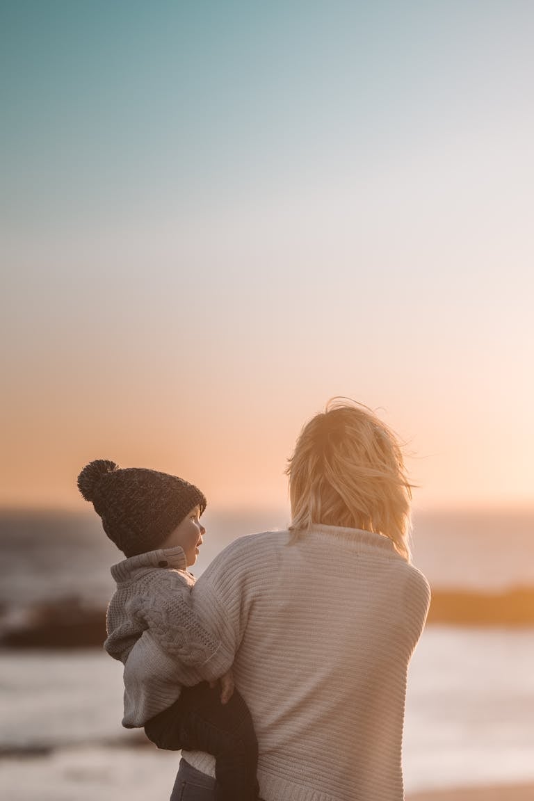 A mother and child share a tender moment on the beach during sunset.