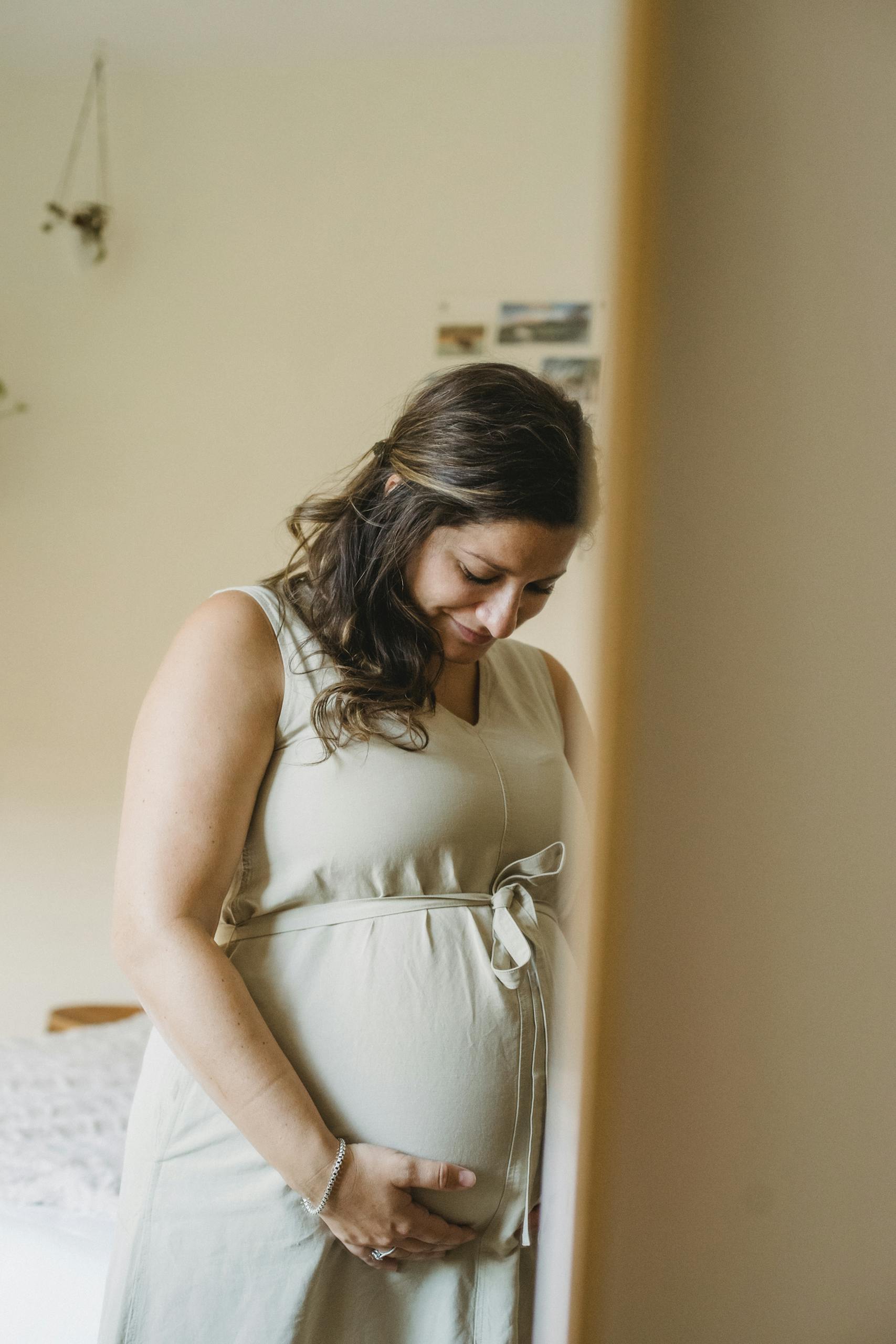 Adult pregnant lady reflection in mirror while standing in room and touching belly in daytime