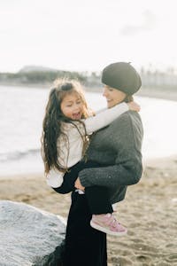 Happy mother holding daughter by the seaside, enjoying a sunny day at the beach.