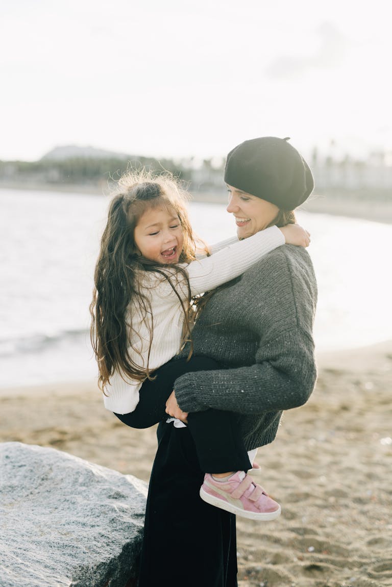 Happy mother holding daughter by the seaside, enjoying a sunny day at the beach.